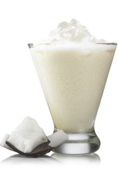 a tall glass filled with whipped cream next to a spoon and sugar cube on a white background