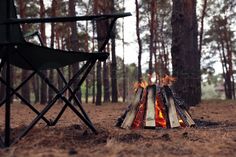 a campfire in the middle of a forest with two chairs around it and trees