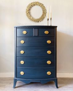 a blue dresser with gold knobs and a wreath on top, against a white wall