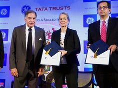 three men and two women standing on stage holding papers in front of a screen with the tata trust logo behind them