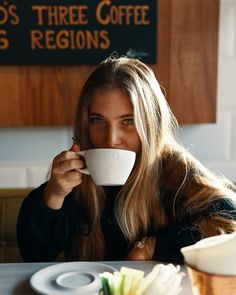 a woman sitting at a table drinking from a cup