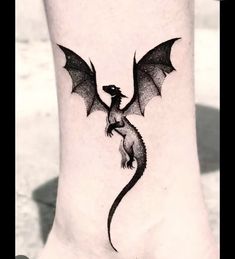 a small black dragon tattoo on the side of someone's foot and it looks like they are flying