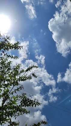 the sun shines brightly through the clouds above some trees and power lines on a sunny day