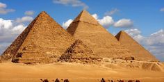 three pyramids in the desert under a blue sky with white clouds and some people