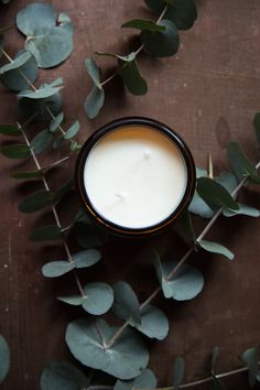 a candle surrounded by eucalyptus leaves on a wooden table