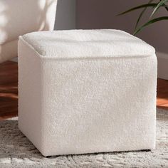 a white ottoman sitting on top of a rug next to a chair and potted plant