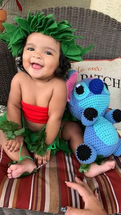 a baby sitting on a chair next to two crocheted stuffed animals and smiling at the camera