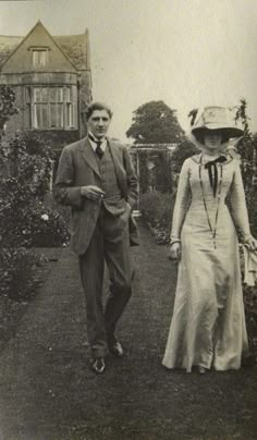 an old black and white photo of a man and woman walking down a garden path