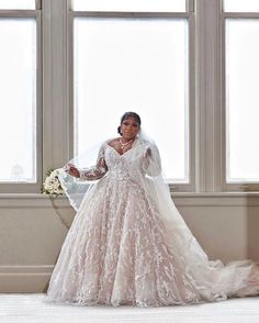 a woman in a wedding dress is standing by a window with her arms out to the side