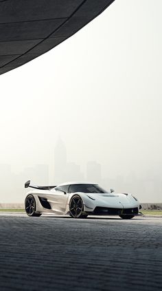 a white sports car parked in front of a large building with a city skyline behind it