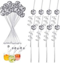 several cocktail stirrers and some drinks on a white table with silver balls in them