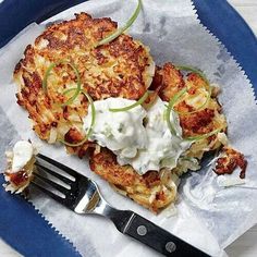 two crab cakes with sour cream and green onions on a blue plate next to a fork