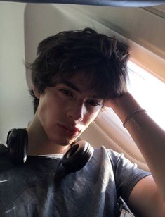 a young man with headphones on his ears looking out an airplane window at the sun