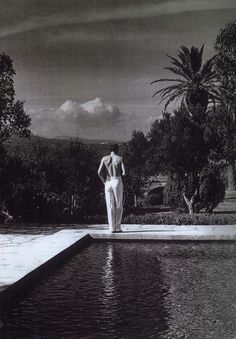 a black and white photo of a woman standing in front of a pool