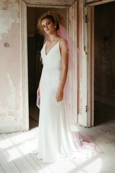 a woman in a white wedding dress is standing by an open door with a pink veil on her head