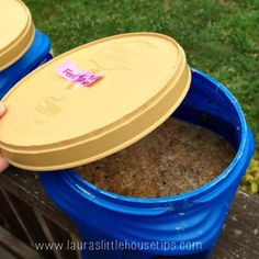 two blue buckets with food in them sitting on a wooden bench next to grass