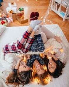 three young women laying on a bed with christmas lights around them and presents in the background