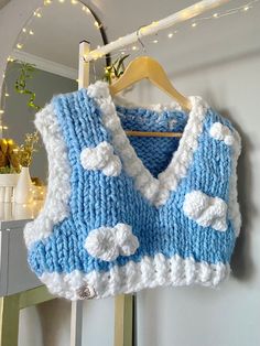 a blue and white knitted sweater hanging on a wall next to a vase with flowers