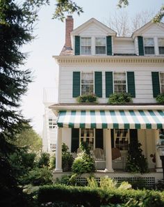 a large white house with green shutters and a striped awning on the front porch