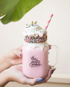 a person holding a pink cup with whipped cream and sprinkles on it