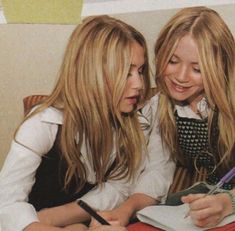 two young women sitting next to each other at a table with notebooks and pens