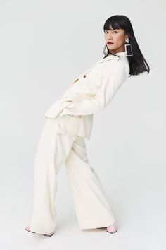 a woman with long black hair wearing white pants and a blazer, posing for the camera