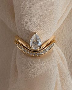 a gold ring with a pear shaped diamond in the center on top of a beige cloth