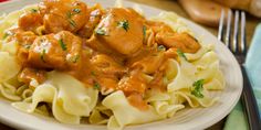 a white plate topped with pasta and meat covered in gravy on top of a wooden table