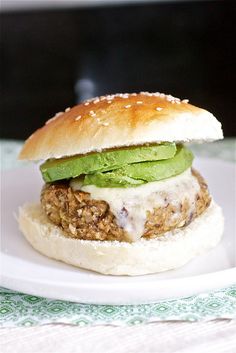 a sandwich with meat, lettuce and cheese on a bun sitting on a white plate