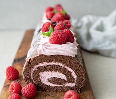 a chocolate roll with raspberries and cream frosting is on a cutting board