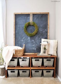 a chalkboard with some baskets underneath it and a wreath hanging on the wall above