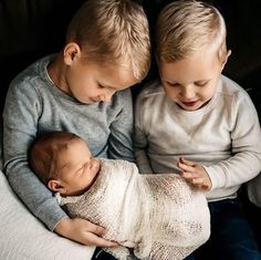 two young boys sitting next to each other holding a baby