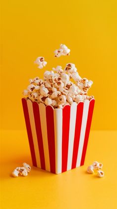 a red and white striped popcorn bucket on a yellow background with scattered popcorn kernels