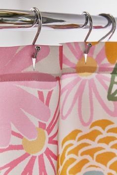 two pink and yellow flowered curtains hanging from a metal rod