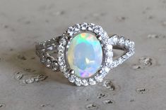 "A lovely Halo Setting featuring an oval-shape genuine top-notch Welo Opal with a magnificent play of color, complemented with a split shank embellished with pave set cubic zirconia handcrafted in Sterling Silver. Wrapped in a box ready for gift-giving.(r-egt-70 ) FINAL SALE Ring Info ----------------- *Opal measure 6mm x 8mm *Opal with Halo measure 11.5mm x 10mm *Ring Shank Width 2mm *Stone height 8mm *Model ring size 5 HOW TO CARE FOR YOUR OPAL --------------------------------------------- Opa Moissanite Opal Engagement Ring, Dazzling Oval Opal Ring, Oval Opal Ring With Gemstone Accents For Anniversary, Dazzling Oval Opal Ring For Anniversary, Oval Opal Ring With Accent Stones, Oval Promise Ring, Juelz Santana, Opal Promise Ring, Rose Gold Opal Ring