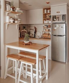 a kitchen with a table and stools next to a refrigerator in the corner,