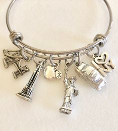 "New York City charm bangle with detailed pewter charms on stainless steel adjustable bangle. Fun detailed pewter charms of famous New York landmarks are 3D or two-sided made in USA and lead and nickel free. They include the Brooklyn Bridge, Empire State Building, apple, Statue of Liberty, taxi and \"I love NY\" charm. Adjustable bangle is made of high quality 1.8mm stainless steel and measures 2.5\" diameter to fit most sizes. Perfect souvenir of trip to NYC!" Nickel-free Metal Bangle Charm Bracelet, Adjustable Antique Silver Metal Bangle, Adjustable Silver Bangle With Charms, Silver Nickel-free Bracelet Souvenir, Nickel-free Silver Bracelets As Souvenir, Adjustable Nickel-free Stainless Steel Bangle, Adjustable Stainless Steel Nickel-free Bangle, New York Souvenirs, Ny Aesthetic