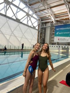 two women in swimsuits standing next to each other near a swimming pool with a sign on the wall