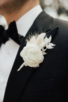 a man wearing a black tuxedo with white flowers on it's lapel