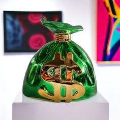 a green glass bottle sitting on top of a white pedestal in front of art work