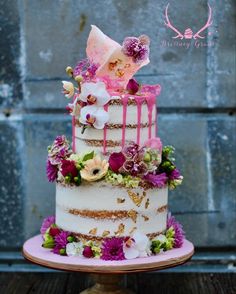 a three tiered cake with pink and purple flowers on top is sitting on a table