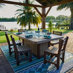 an outdoor dining table and chairs on a blue rug with palm trees in the background