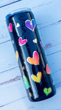 a black cup with hearts painted on it sitting on a white wooden table next to a wall