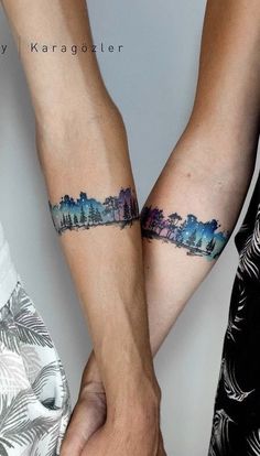 two people are holding hands with tattoos on their arms and one is showing the city