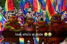 some people are standing in the street with colorful flags and banners behind them, one person is holding a sign that says look who's at pride