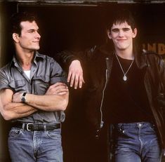 two young men standing next to each other in front of a building with their arms crossed