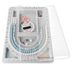 an assortment of jewelry is displayed in a plastic tray on a white surface with scissors and beads