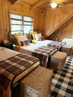 three beds in a room with wooden walls and plaid blankets on the bedding, along with two stools