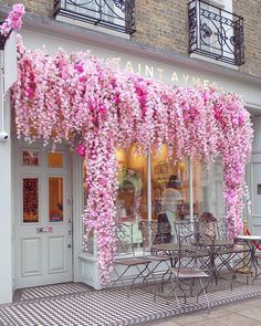 pink flowers are growing on the outside of a storefront in front of a table and chairs