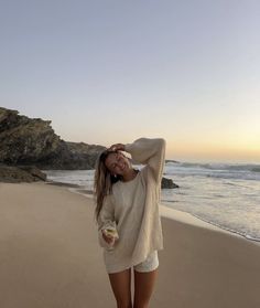 a woman standing on top of a beach next to the ocean holding a glass of wine